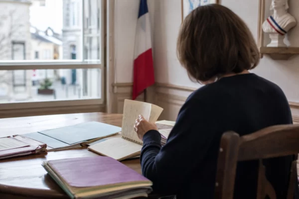 Élu local anonyme de dos dans une mairie, carnet et dossier en main, lumière naturelle de fin de journée.