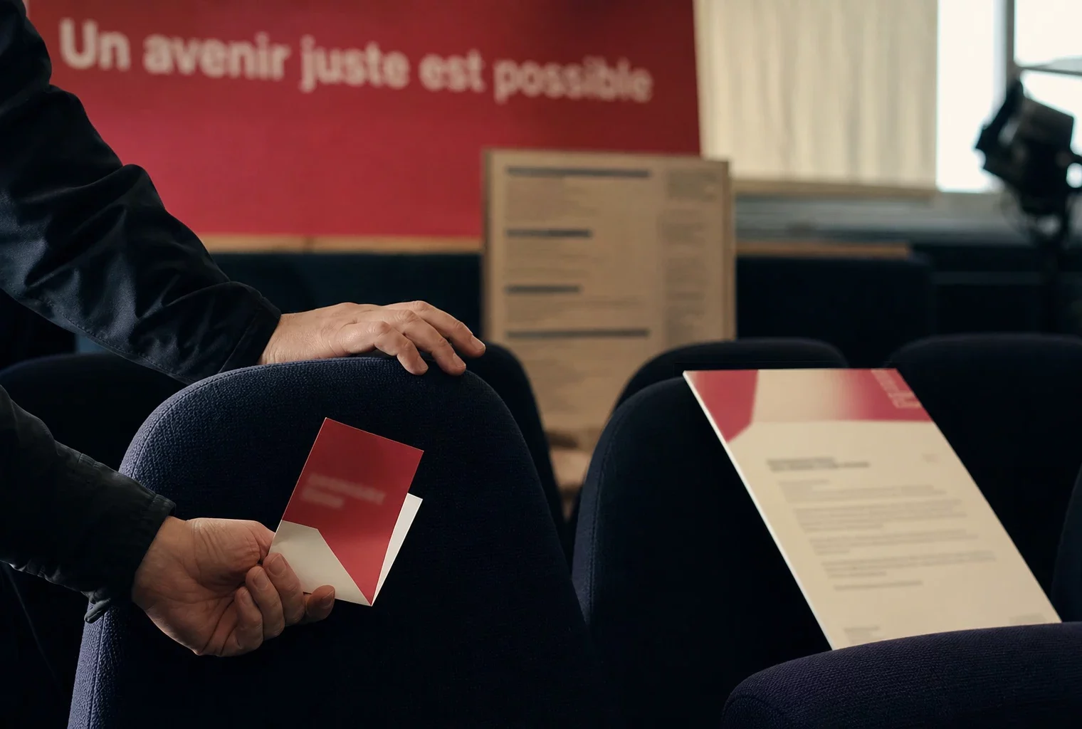 Main sur un fauteuil de salle avec billet flou et programme culturel en arrière-plan, lumière naturelle chaude.