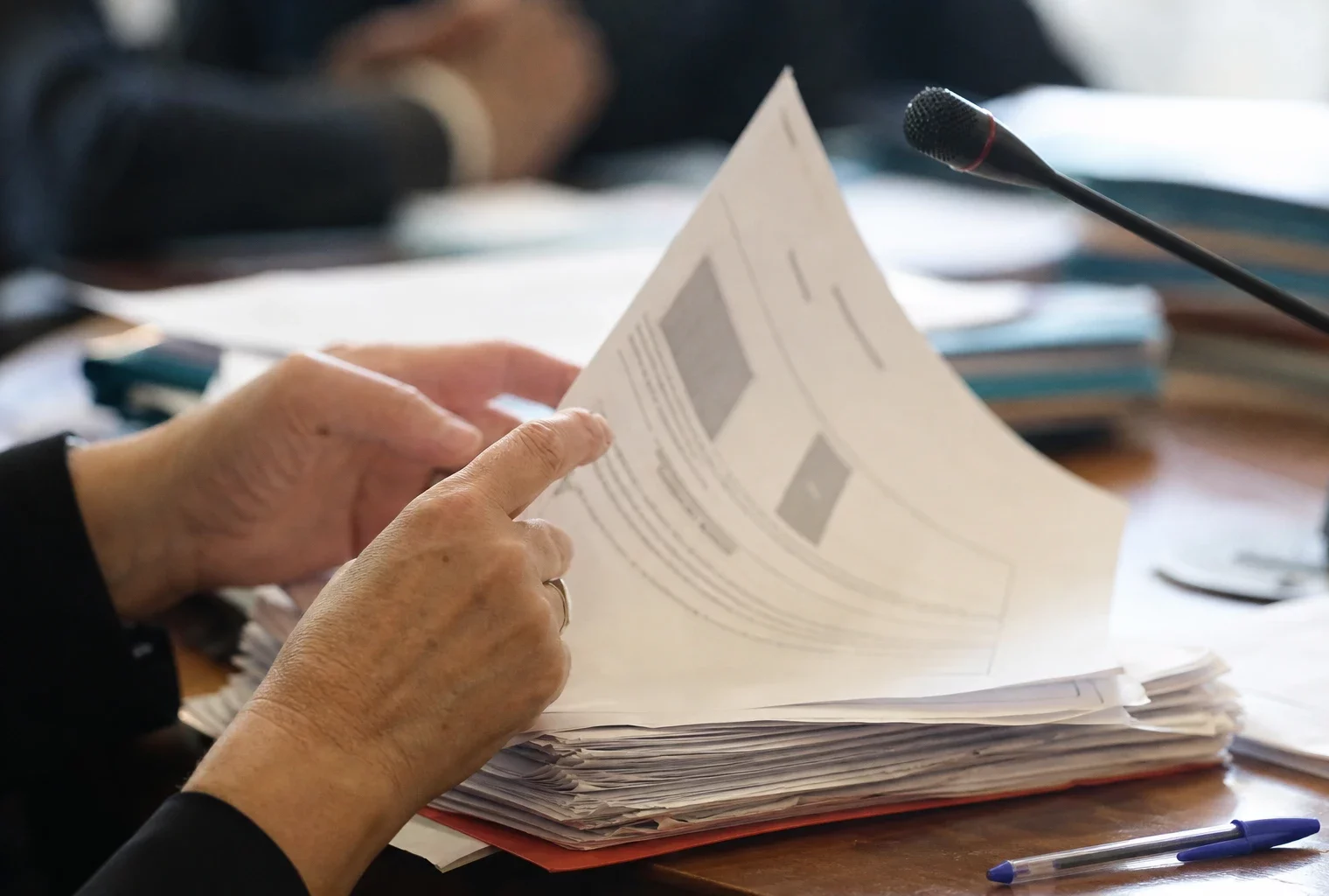 Mains anonymes feuilletant un dossier devant un micro de commission dans un cadre institutionnel français