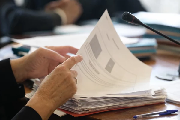 Mains anonymes feuilletant un dossier devant un micro de commission dans un cadre institutionnel français