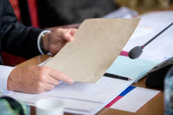 Dossier de commission parlementaire tenu par des mains anonymes, avec micro et documents flous sous lumière naturelle.