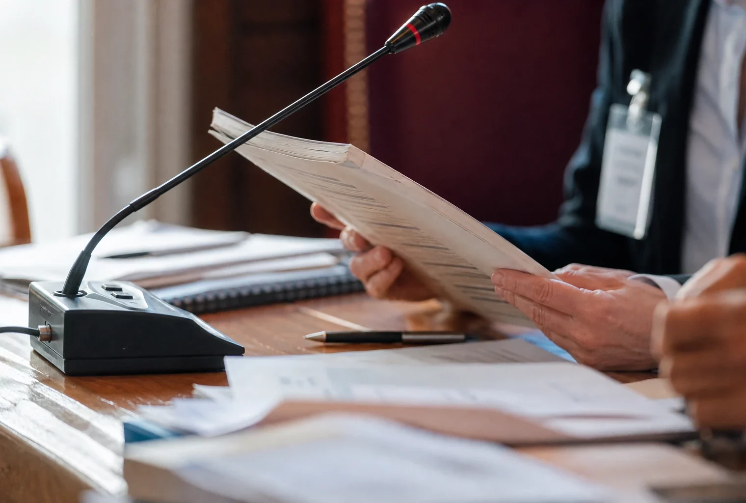 Mains anonymes tenant un dossier devant un micro de commission dans un cadre institutionnel français lumineux