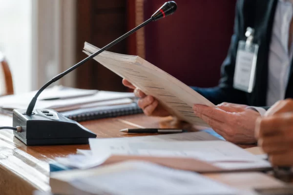Mains anonymes tenant un dossier devant un micro de commission dans un cadre institutionnel français lumineux