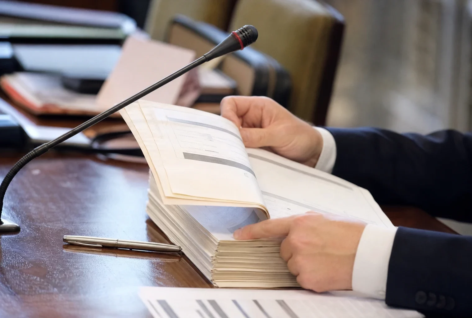 Dossier d’audition tenu par des mains anonymes avec micro de commission dans une salle parlementaire floue