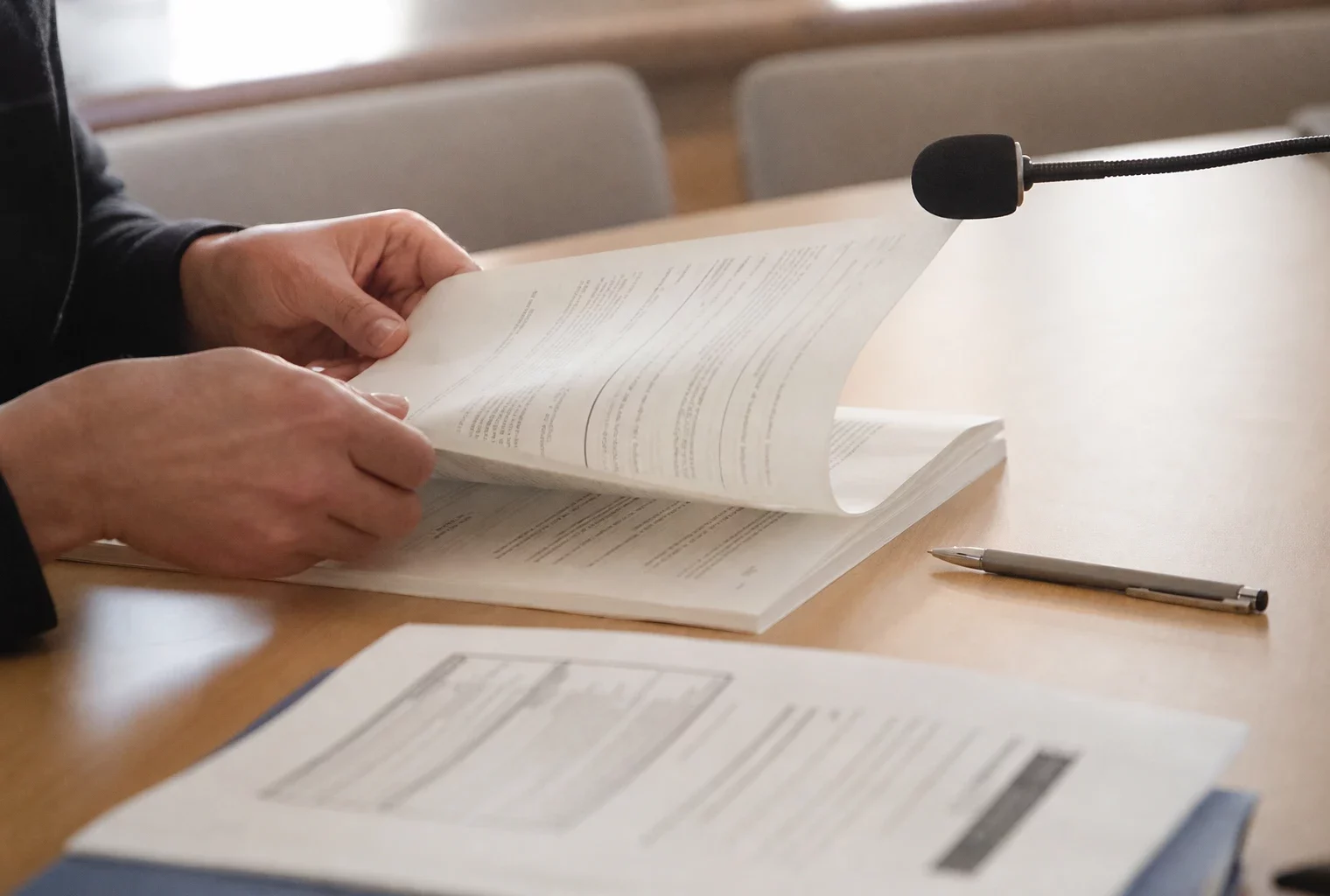 Mains anonymes feuilletant un dossier de nomination devant un micro de commission parlementaire