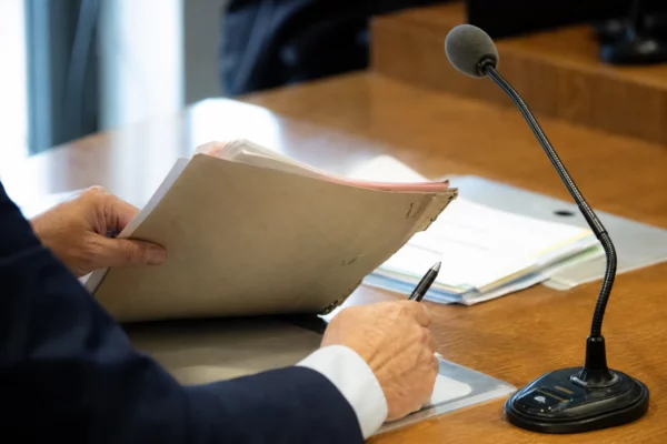 Mains anonymes tenant un dossier lors d’une audition parlementaire, avec micro de commission et documents flous.
