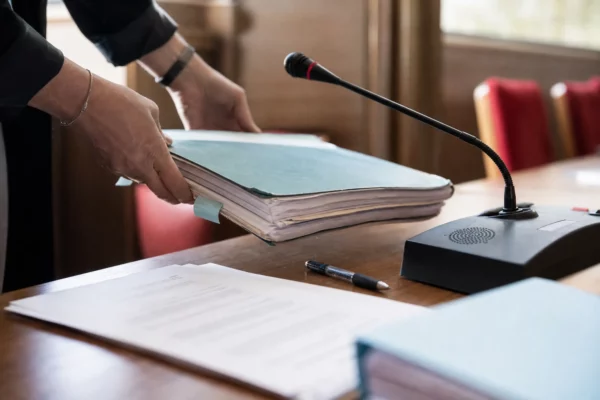 Dossier parlementaire et micro de commission sur une table, mains anonymes dans une salle institutionnelle lumineuse