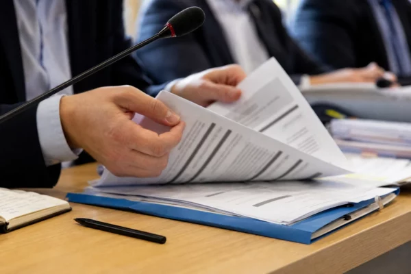 Mains anonymes près d’un micro et d’un dossier de nomination dans une salle de commission régionale