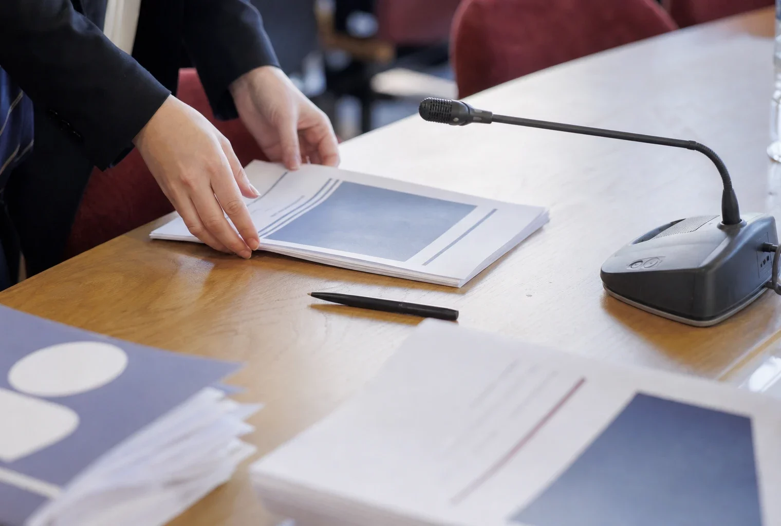 Dossier d’audition, micro de commission et mains anonymes dans une salle parlementaire française.