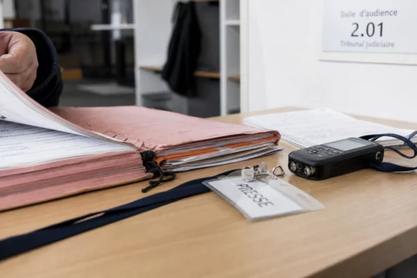 Dossier judiciaire ouvert, badge de presse et enregistreur audio sur une table, dans une lumière claire d’intérieur