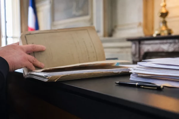 Main tenant un dossier judiciaire à côté de notes de campagne dans un bureau lumineux, ambiance politique et juridique française.