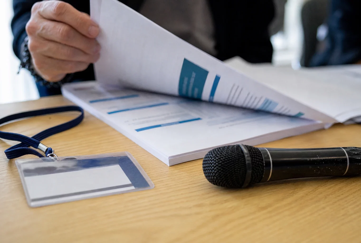 Gros plan d’un dossier institutionnel et d’un micro de presse sur une table, avec une main en train de feuilleter un document.
