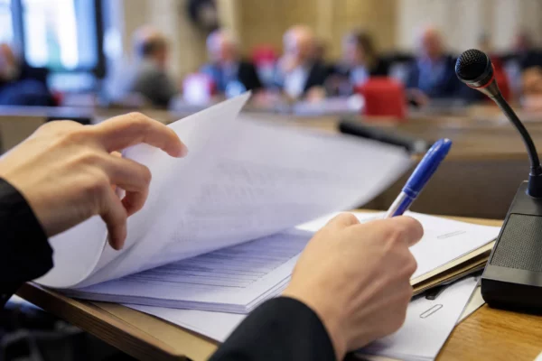 Dossier de nomination examiné à la commission, avec micro de table et mains anonymes dans une lumière claire.