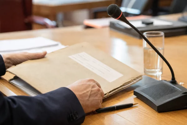 Main anonyme préparant un dossier de nomination près d’un micro de commission dans une salle institutionnelle lumineuse.