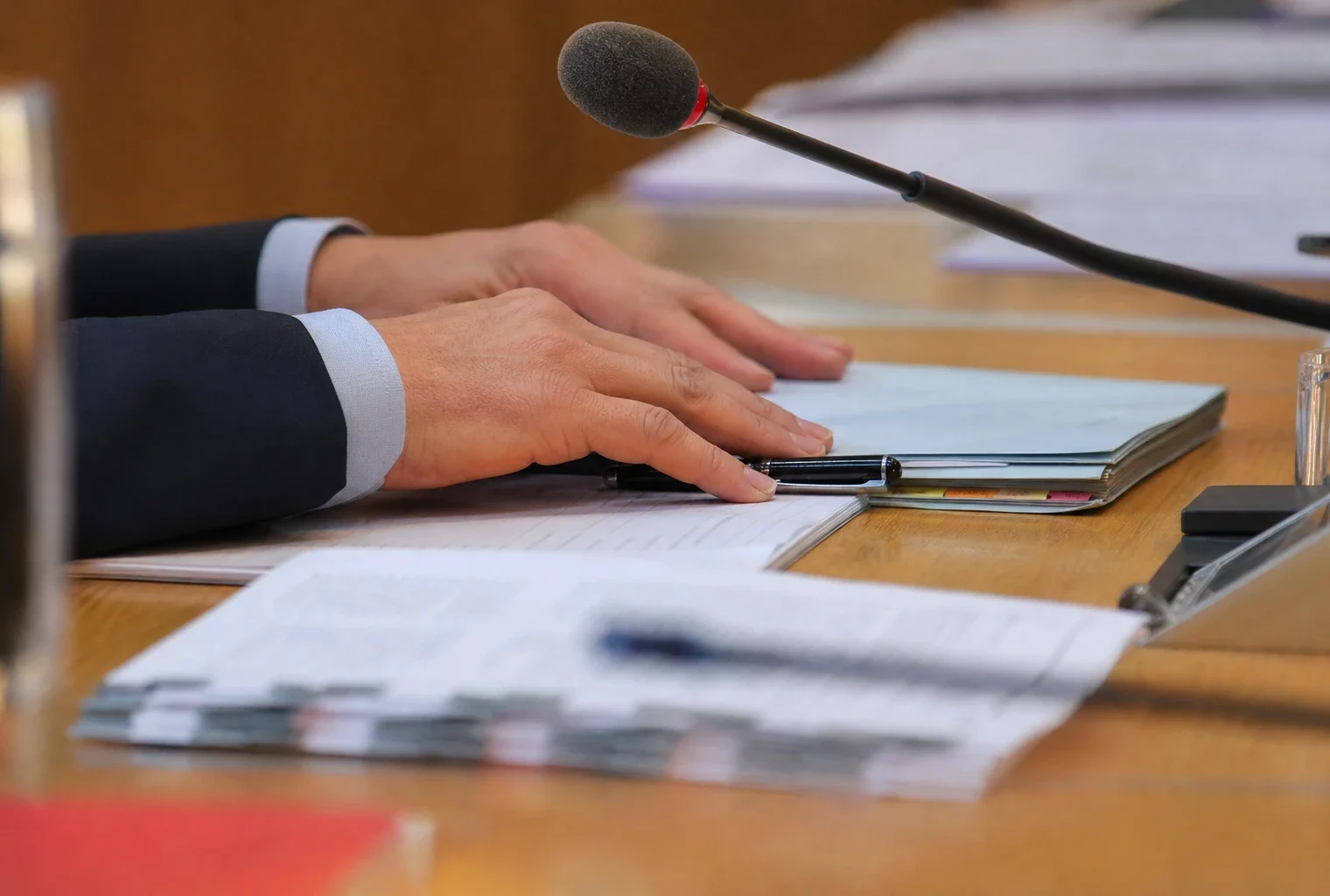 Dossier de nomination examiné à une commission, avec micros, stylo et mains anonymes dans une lumière claire.