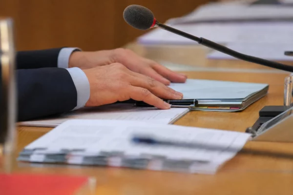 Dossier de nomination examiné à une commission, avec micros, stylo et mains anonymes dans une lumière claire.