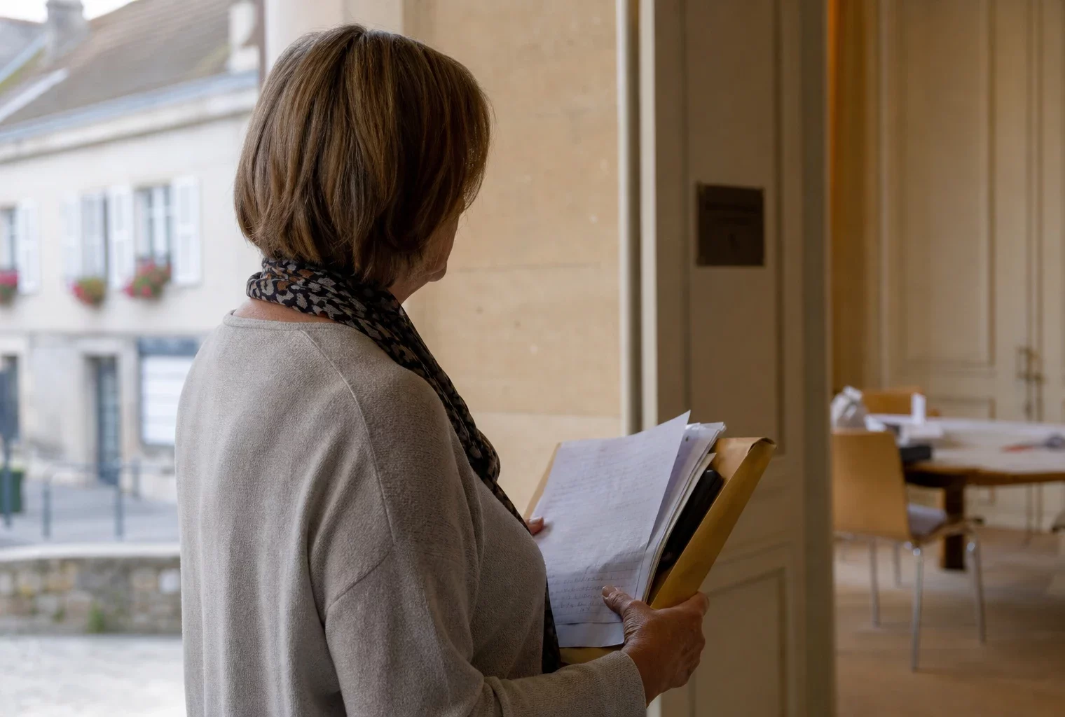 Un élu local anonyme de dos consulte un dossier dans un couloir de mairie, lumière naturelle et ambiance civile.