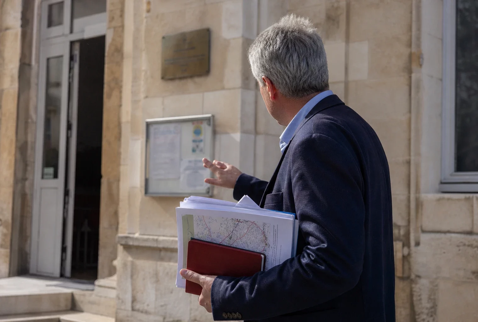 Élu local anonyme devant une mairie française, tenant un dossier lié à une grande course cycliste.