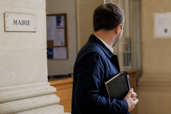 Élu local anonyme dans le hall lumineux d’une mairie, carnet et dossier à la main, en portrait de presse