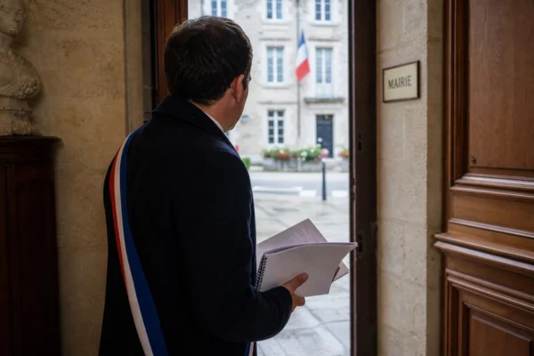 Élu local anonyme de dos dans un couloir de mairie, carnet en main, avec la rue civique en arrière-plan.