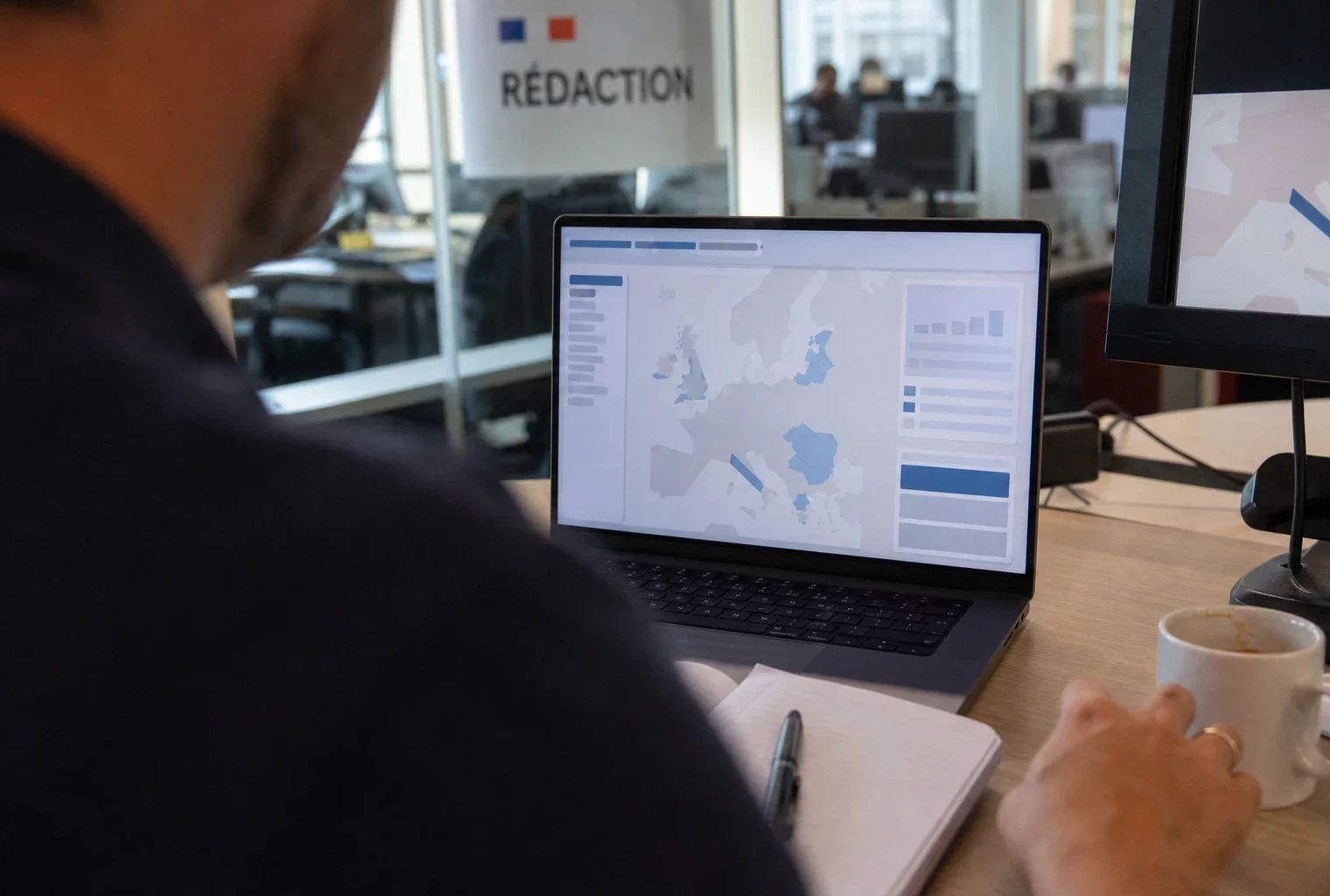 Vue de dos sur un ordinateur affichant une interface européenne abstraite, avec une main floue au premier plan.