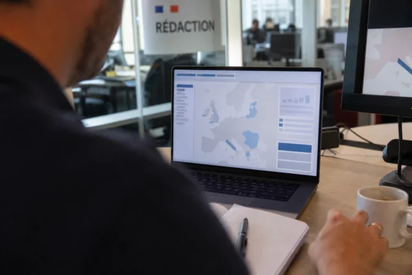 Vue de dos sur un ordinateur affichant une interface européenne abstraite, avec une main floue au premier plan.
