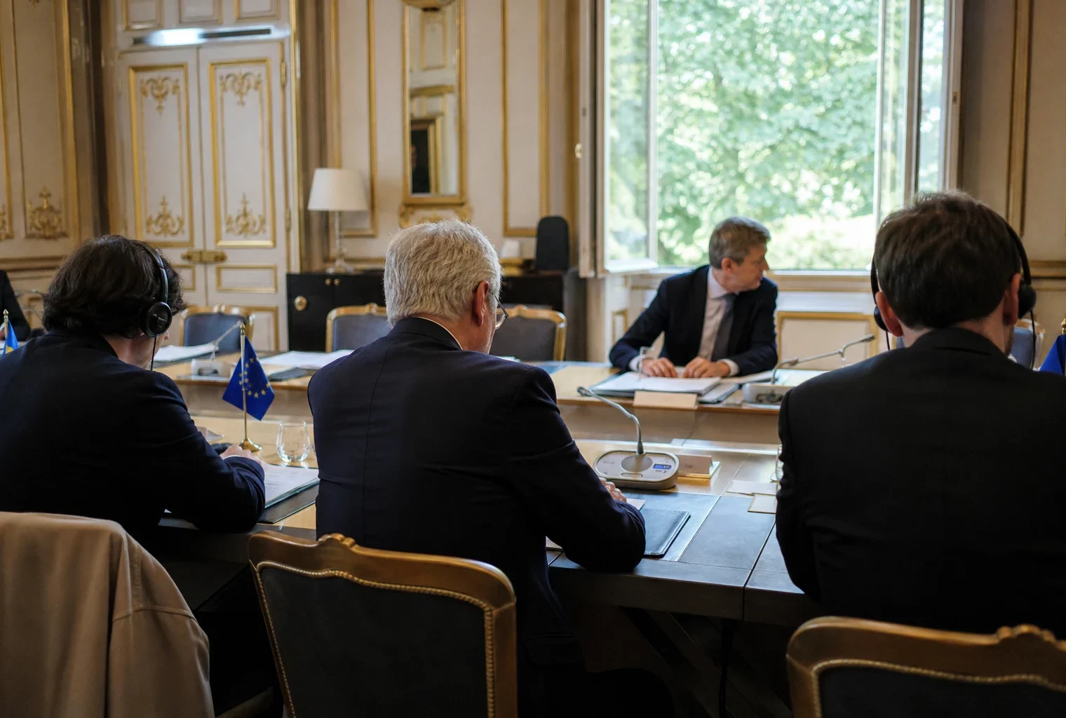 Réunion institutionnelle européenne sobre avec dossiers et drapeaux de table discrets, en lumière naturelle claire