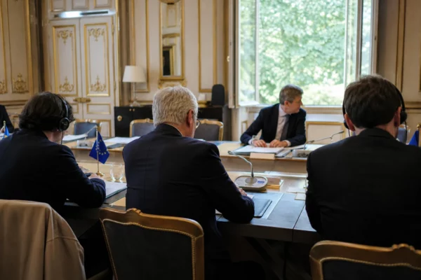 Réunion institutionnelle européenne sobre avec dossiers et drapeaux de table discrets, en lumière naturelle claire