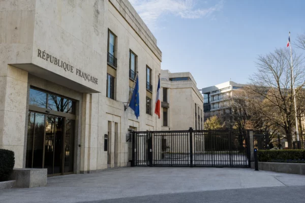 Façade d’un bâtiment diplomatique français à Washington, vue oblique, avec drapeau tricolore discret et lumière naturelle claire.