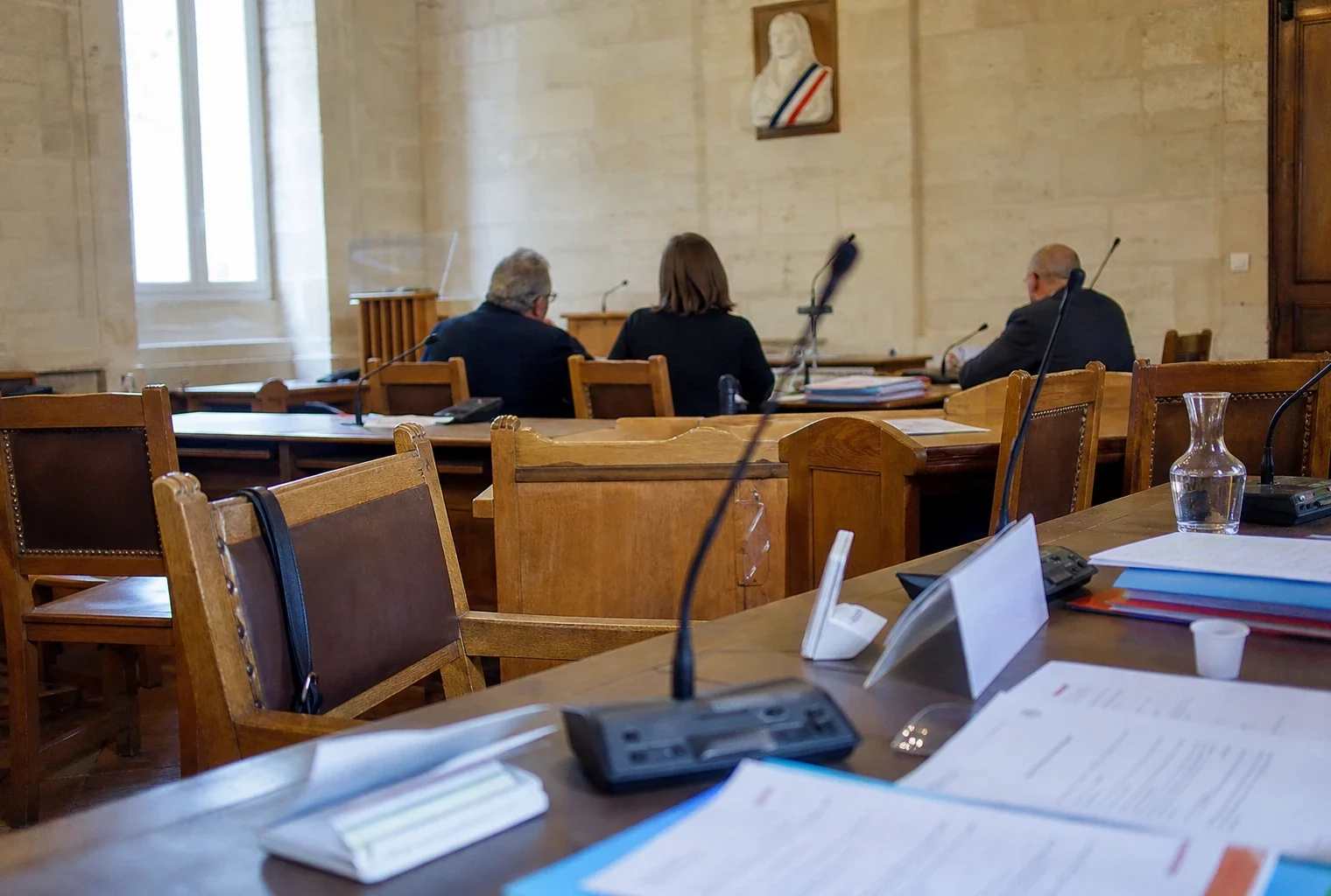 Salle municipale avec micros, dossiers flous et chaise vide lors d’un débat local sur la fin de vie