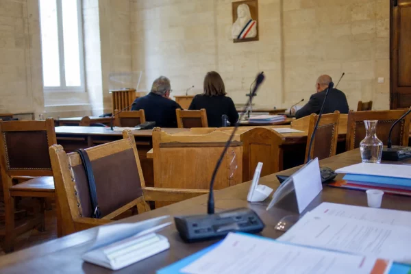 Salle municipale avec micros, dossiers flous et chaise vide lors d’un débat local sur la fin de vie