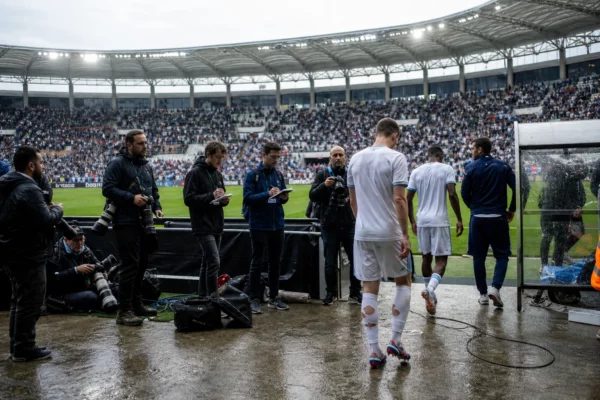 Des journalistes attendent en zone mixte après un match de Coupe du monde 2026, avec des joueurs anonymes au stade.