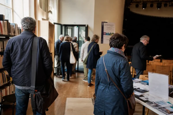 Foyer d’un lieu culturel municipal à Paris avec visiteurs anonymes et brochures floues après un débat public.