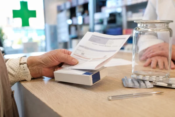 Gros plan dans une pharmacie française sur une main tenant un reçu et une boîte de médicament