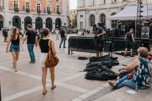 Place de Grenoble après un concert interrompu, avec techniciens, câbles et passants autour d’une scène de festival.