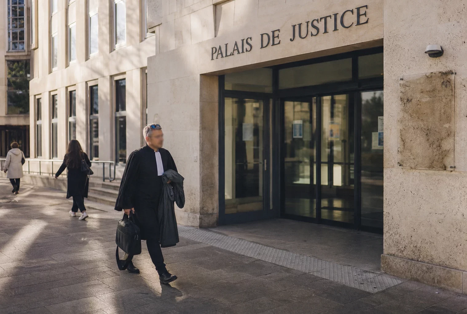 Façade du palais de justice de Grenoble avec passants anonymes devant l’entrée, en lumière naturelle claire.