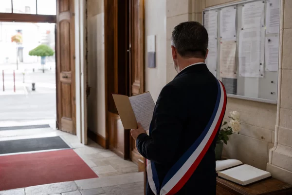Un élu local de dos dans une mairie, tenant un dossier en hommage aux pompiers morts en Gironde.