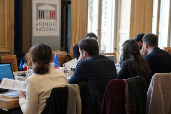 Réunion institutionnelle sobre avec dossiers et micros, silhouettes de dos autour d’une table européenne