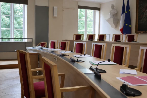 Salle municipale française avec micros et dossiers flous, chaise vide, ambiance sobre liée aux incendies de Fontainebleau