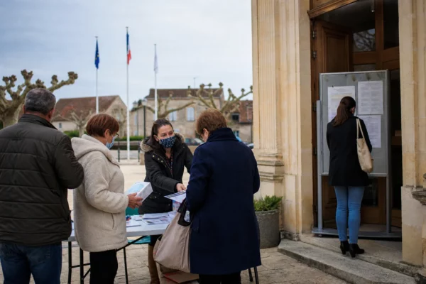 Des habitants et un agent municipal devant une mairie en Gironde, dans une ambiance claire liée aux fumées de l’incendie.