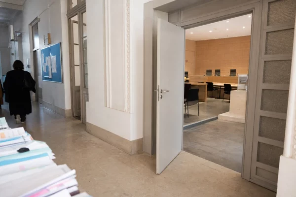 Couloir clair d’un bâtiment institutionnel français, porte sobre et salle d’audition vide en arrière-plan