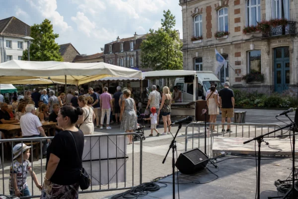 Place de Liévin animée par une fête locale, avec habitants anonymes, stands de quartier et mairie en arrière-plan.
