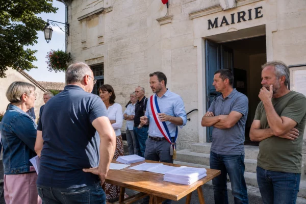 Des citoyens discutent devant une mairie française au sujet des effets d’une loi agricole sur la vie locale.