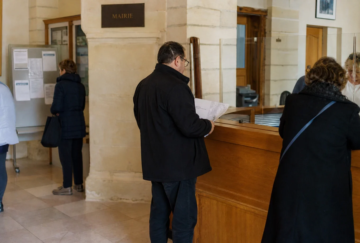 Accueil lumineux d’une mairie française avec des usagers anonymes et un comptoir de service public.