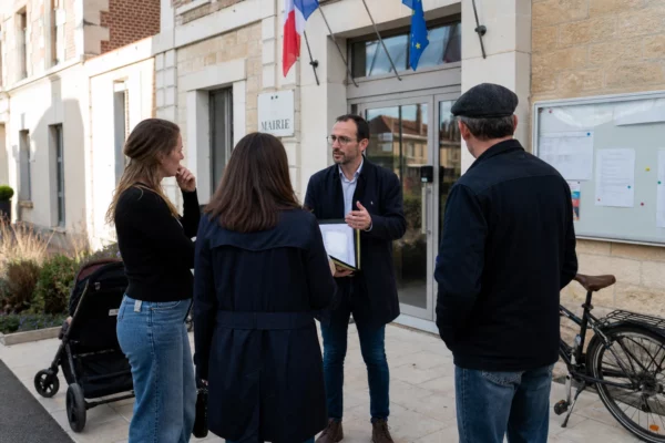 Des habitants discutent devant une mairie française, dans une scène locale liée au débat politique et au bilan présidentiel.