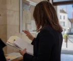 Un collaborateur municipal anonyme consulte un dossier dans un couloir de mairie, lumière naturelle et arrière-plan urbain flou.