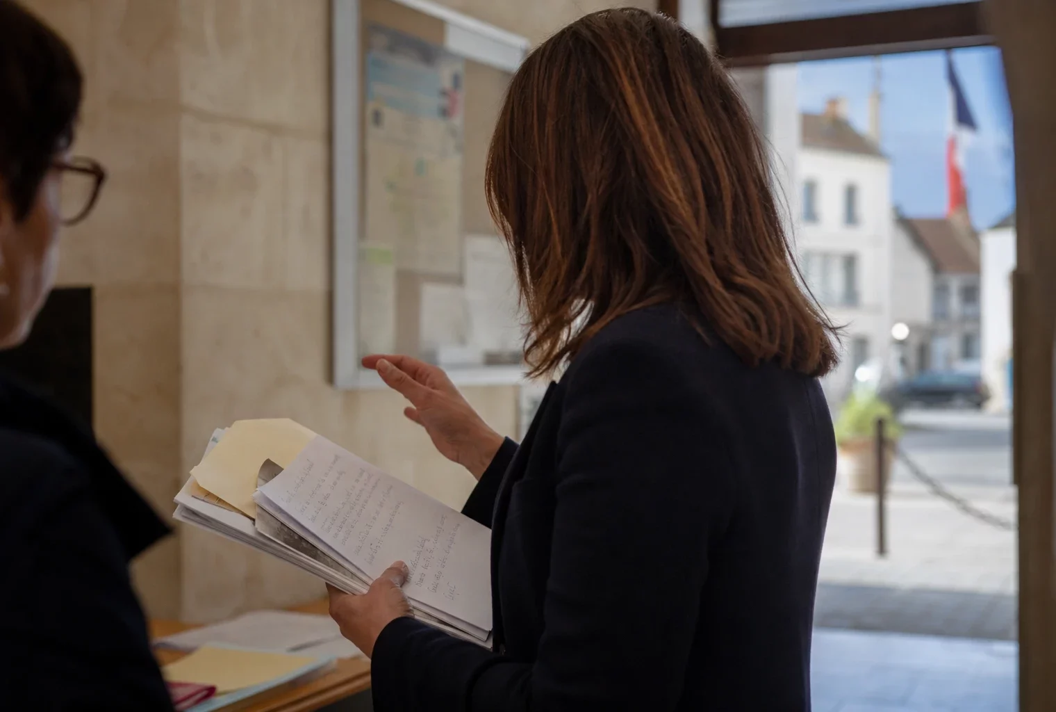 Un collaborateur municipal anonyme consulte un dossier dans un couloir de mairie, lumière naturelle et arrière-plan urbain flou.
