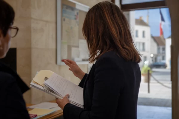 Un collaborateur municipal anonyme consulte un dossier dans un couloir de mairie, lumière naturelle et arrière-plan urbain flou.