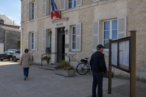 Des passants devant une mairie de ville française, sous une lumière claire, dans une scène civique liée à l’élection.