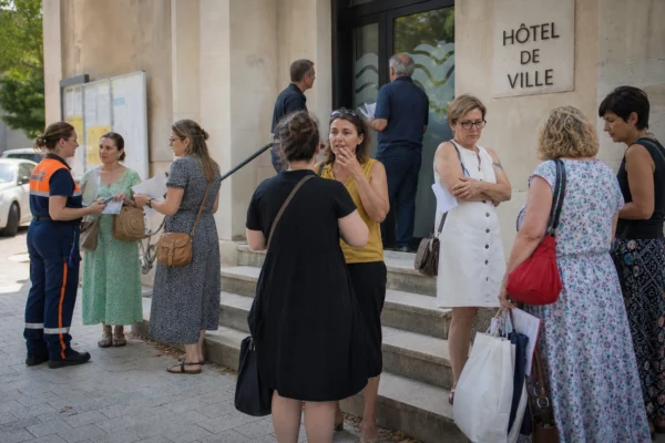 Des habitants et des agents municipaux échangent devant une mairie de province après les alertes aux incendies.
